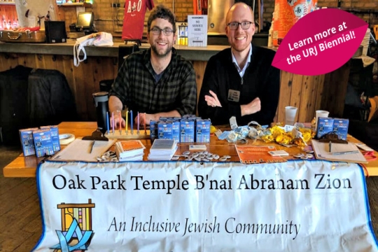 Rabbi Daniel Kirzane and another man sitting at a table with a sign that reads Oak Park Temple Bnai Abraham Zion an Inclusive Jewish Community  