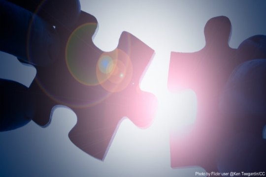 Two puzzle pieces being held in front of bright sunlight