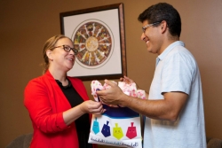 A man and woman exchanging a Hanukkah gift in a bag patterned with colorful dreidels
