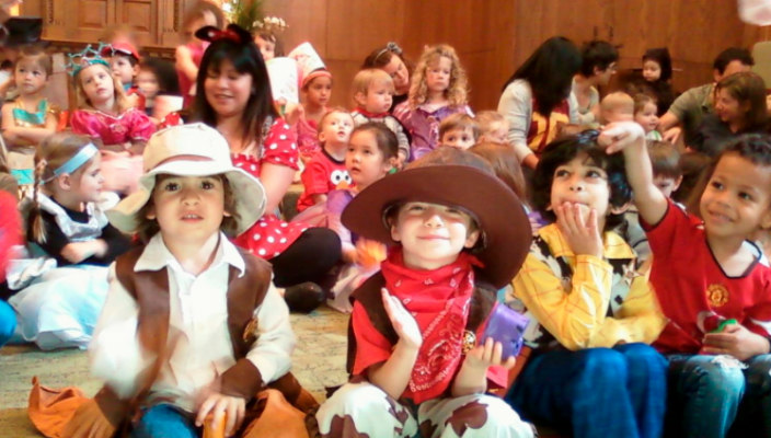 Smiling young children wearing Purim costumes and sitting on the bimah in a synagogue