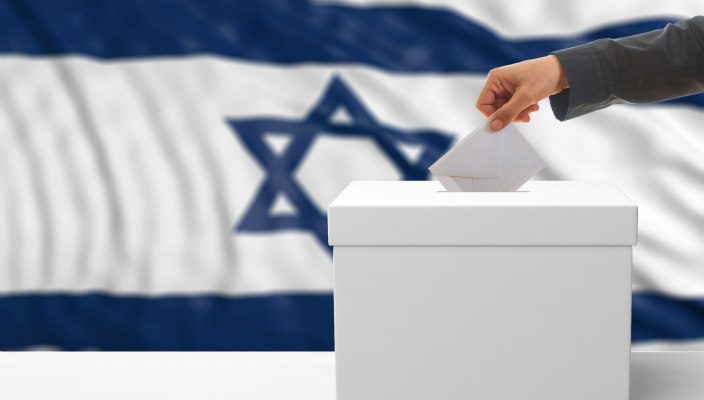 Hand placing a ballot in ballot box; Israeli flag in the background